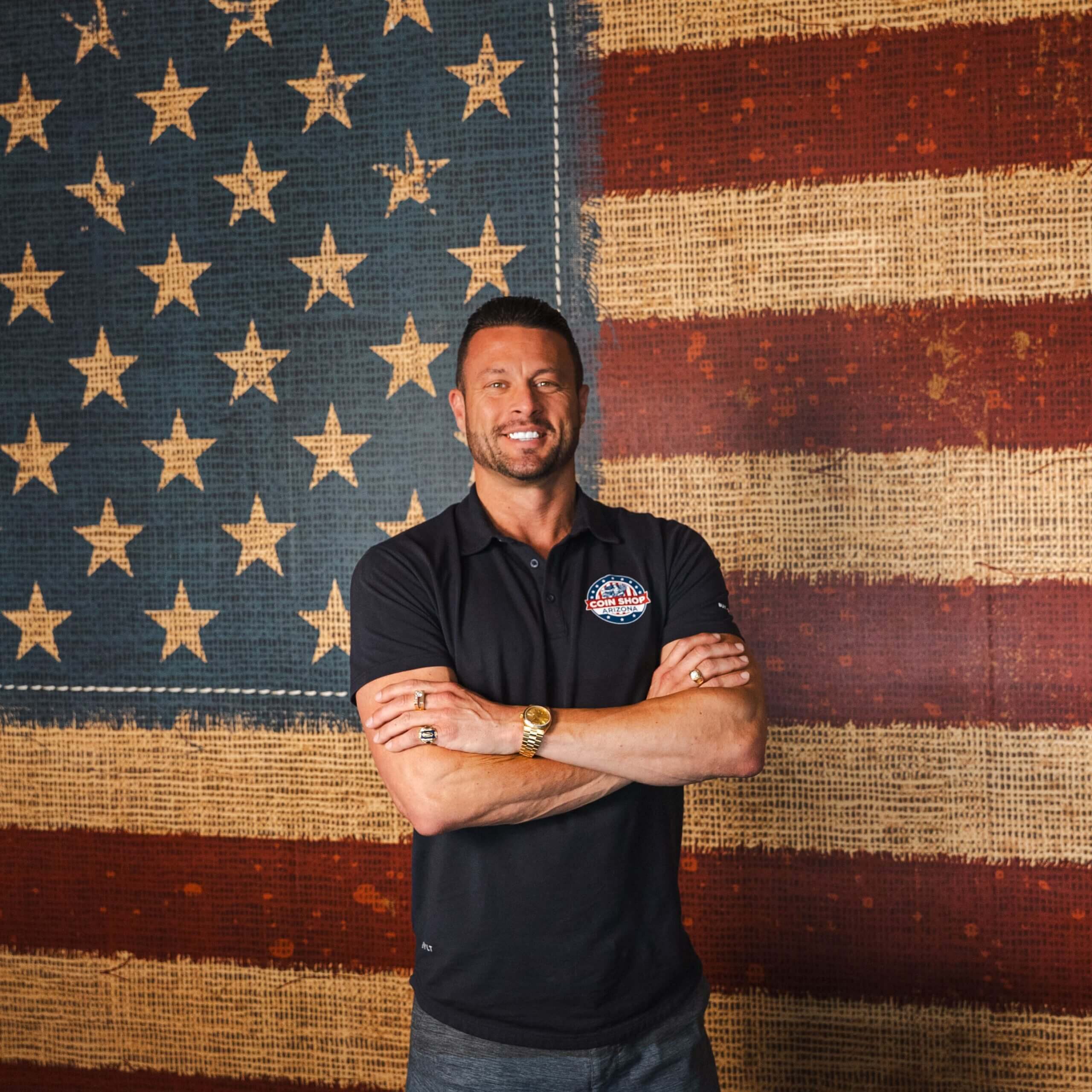 Smiling man with folded arms and flag backdrop
